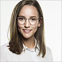 Porträt einer lächelnden Frau mit Brille und braunem Haar vor weißem Hintergrund. Sie trägt ein weißes Hemd.