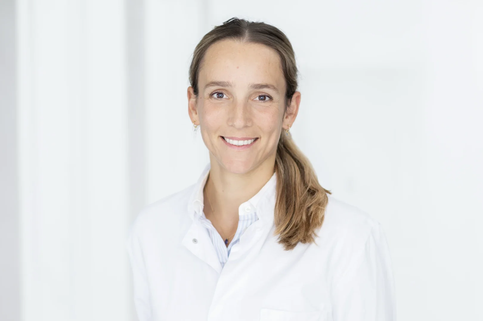 Porträt einer lächelnden Frau mit Brille und braunem Haar vor weißem Hintergrund. Sie trägt ein weißes Hemd.