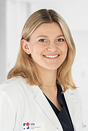 Eine lächelnde Frau in einem weißen Arztkittel in einem hellen Raum.
