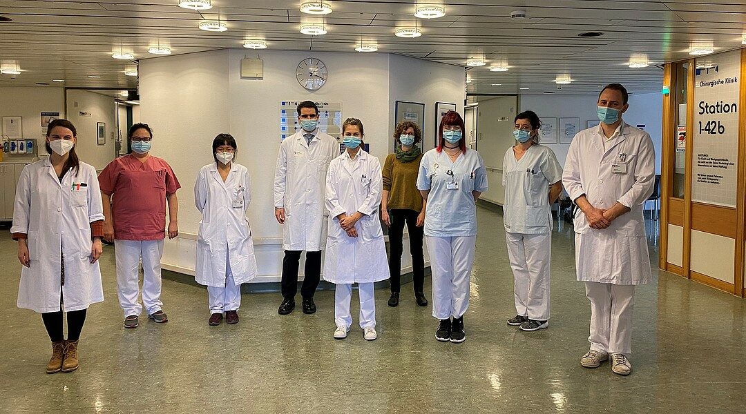 Klinikteam in Schutzkleidung und Masken steht in einem Krankenhausflur.