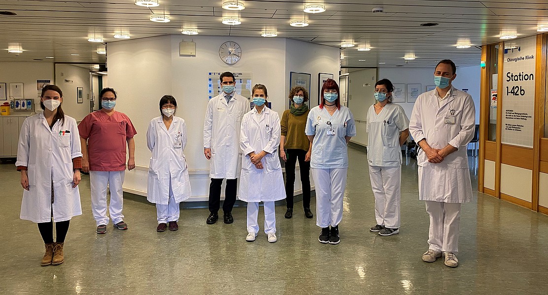 Klinikteam in Schutzkleidung und Masken steht in einem Krankenhausflur.