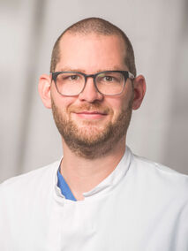 Mann mit Brille und Bart in weißem Kittel lächelt.