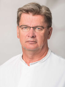Ein Mann mit Brille und weißem Hemd blickt ernst in die Kamera.